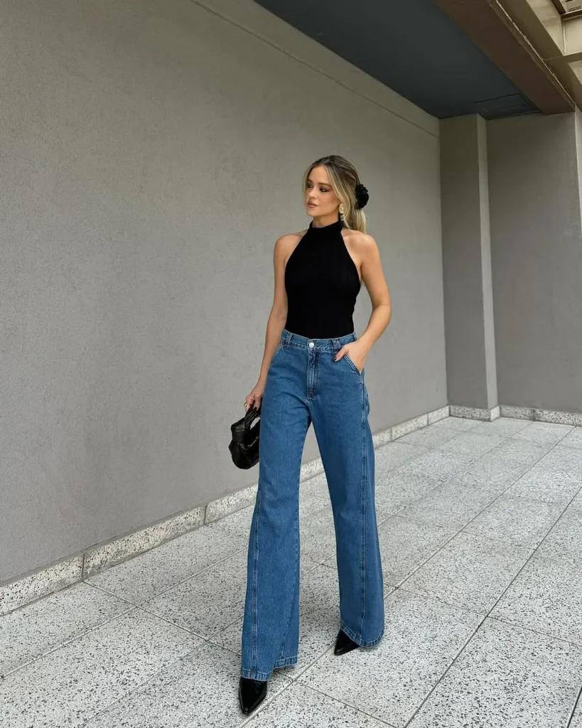 Minimalist classy outfit with a black high-neck sleeveless top and wide-leg denim jeans, styled with pointed black heels and a sleek bun.