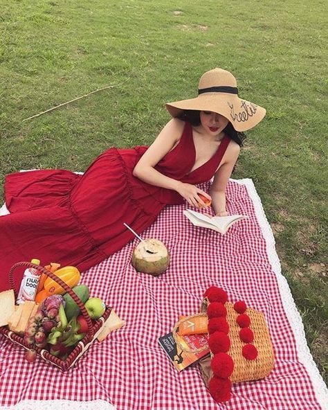 Picnic Date Outfits: Woman in a red dress and wide-brimmed hat reading a book beside a picnic basket filled with fruit.