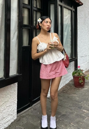 A woman in a white spaghetti strap top and pink mini skirt, accessorized with socks and heels; cute and youthful summer outfit idea.

