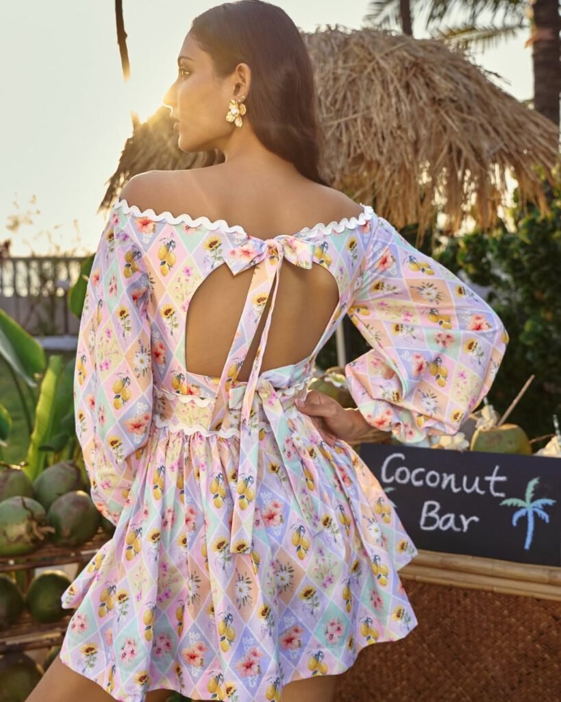 Back view of a woman in a pastel-colored off-shoulder dress with a bow tie and floral prints, showcasing a playful summer outfit verano.