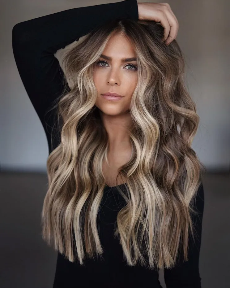 A woman with long, layered brown hair featuring natural highlights, exhibiting a vibrant, sunlit brown hair color idea.