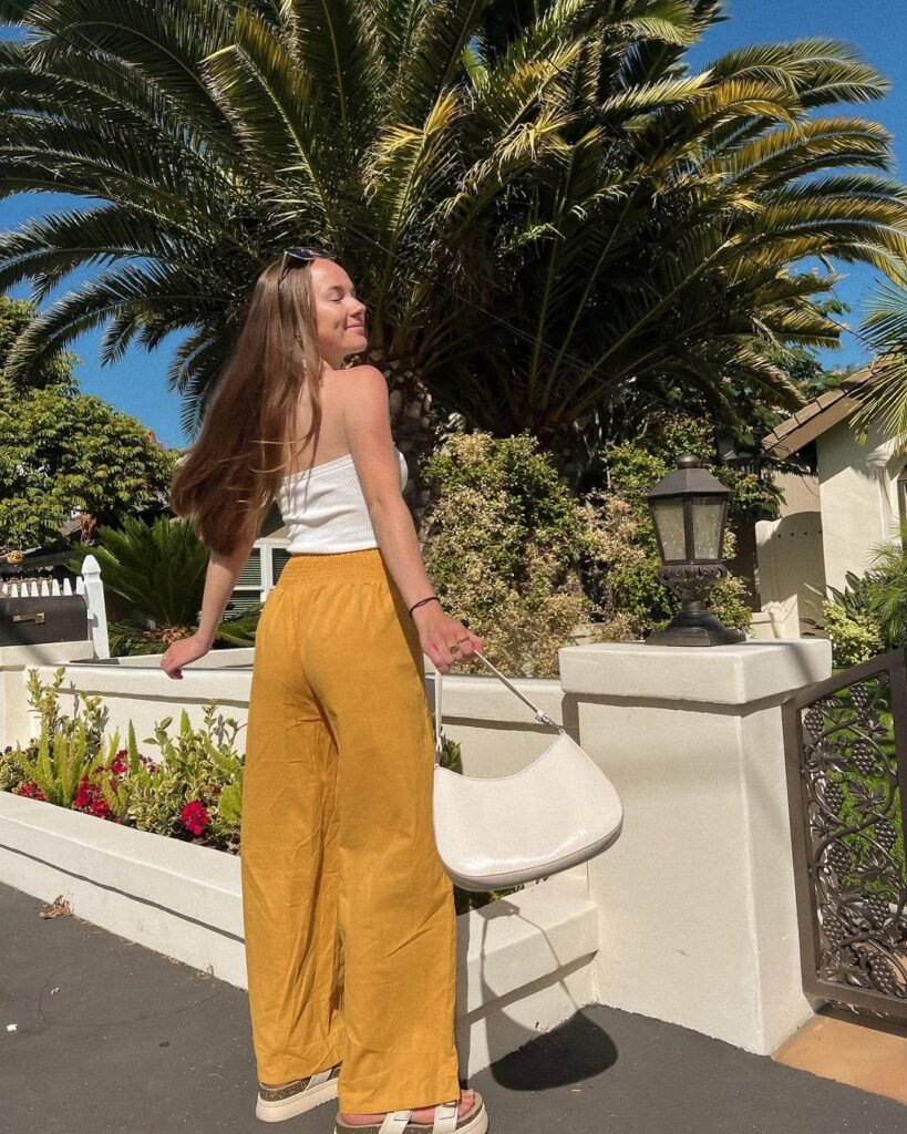 Fashionable linen pant outfit with white linen pants, black crop top, and a loose white shirt, carrying a woven tote bag.