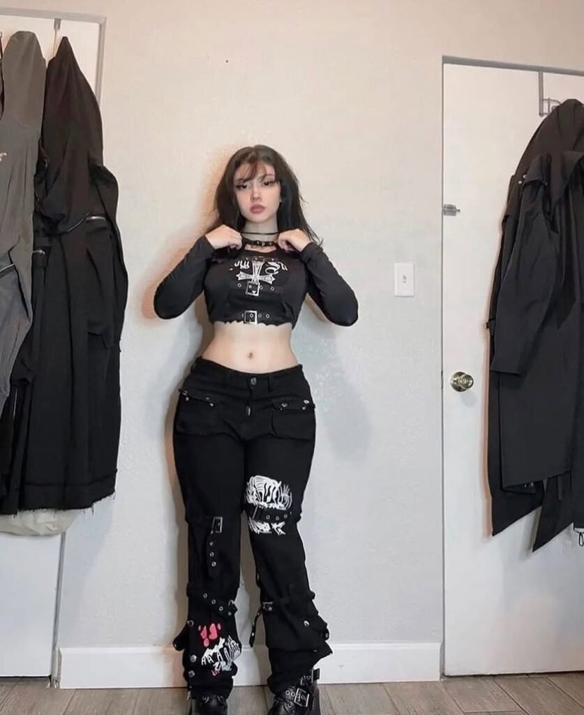 Grunge Outfits: Person with long dark hair wearing a black graphic t-shirt and black leather pants posing against a black and white wall.