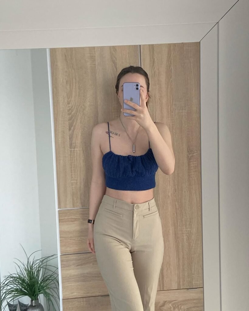  Woman posing in front of a mirror wearing a navy blue crochet crop top with spaghetti straps and beige pants – Crochet Outfits.