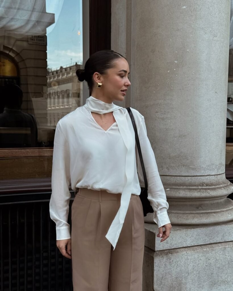 Classy stylish work outfit with a white tie-neck blouse and brown trousers.