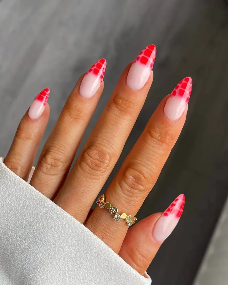 Long almond nails with a nude base and red gradient grid pattern on tips, accessorized with a gold ring, creative Red Nail Ideas.