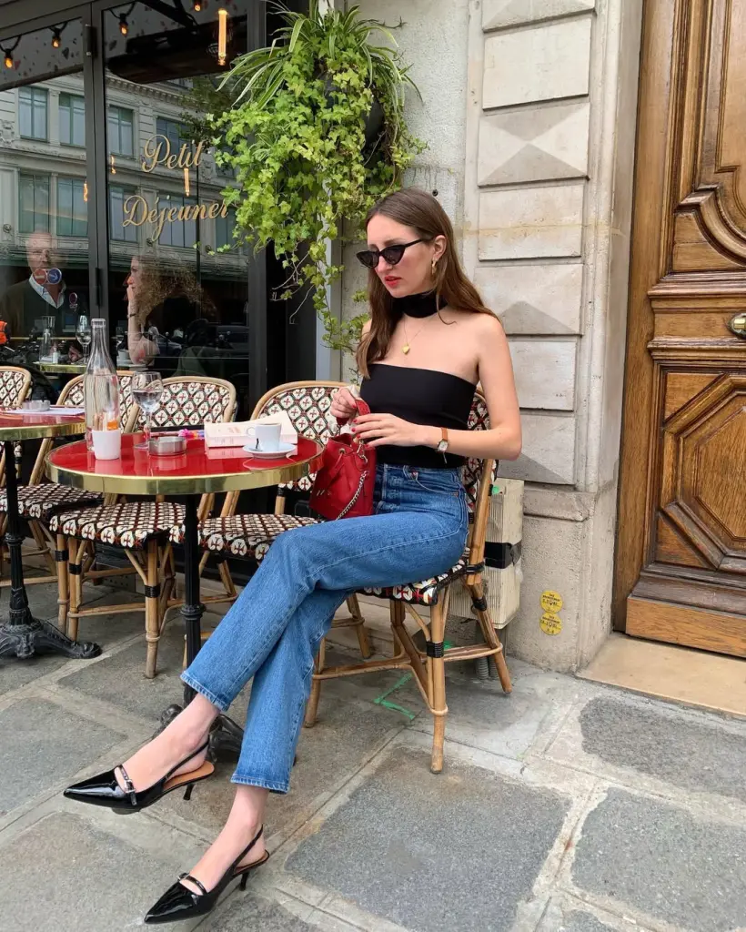  Parisian-inspired classy outfit featuring a black strapless top, straight jeans, and black slingback heels, accessorized with cat-eye sunglasses.