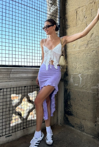 Trendy mix of sporty and feminine featuring a white crop top and a lilac ruffle skirt, completed with sneakers — a playful twist for outfit ideas summer.