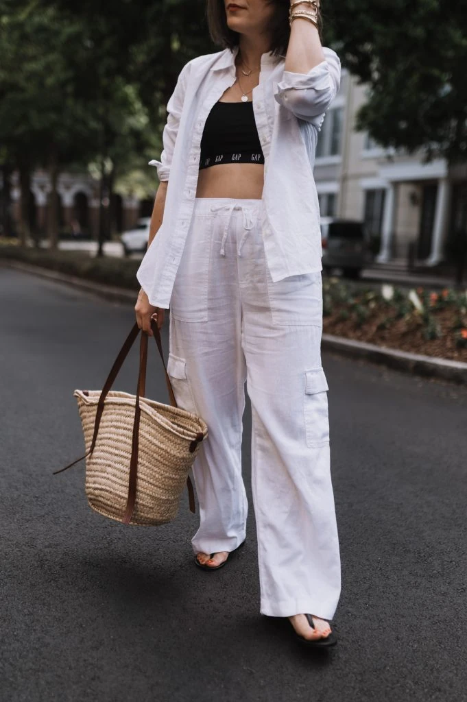 Woman dressed in white ribbed sleeveless top with beige linen pants, carrying a large brown handbag.