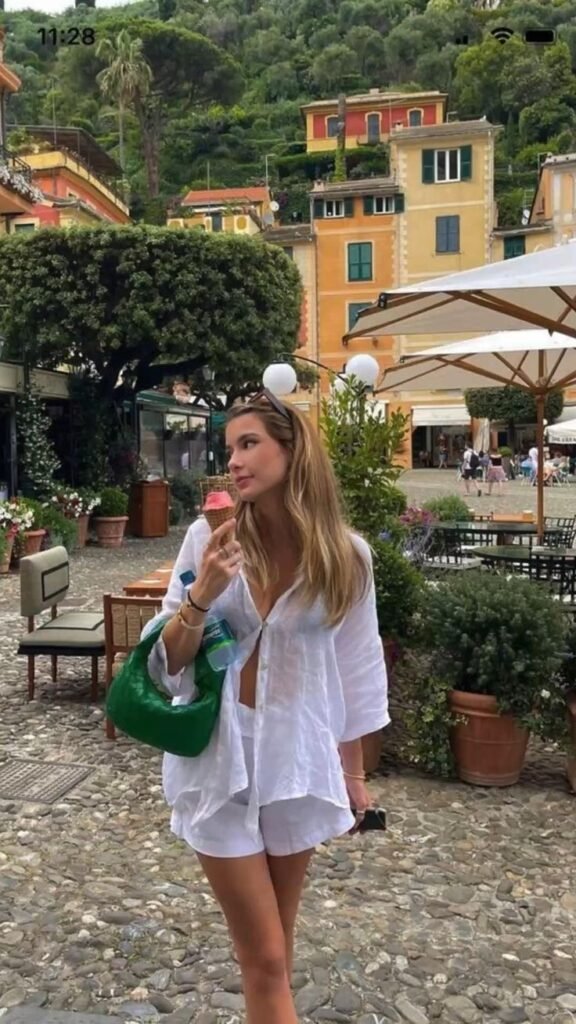 A woman enjoying gelato in Portofino, dressed in a relaxed white linen set with a green handbag, capturing the essence of a laid-back European summer outfit.