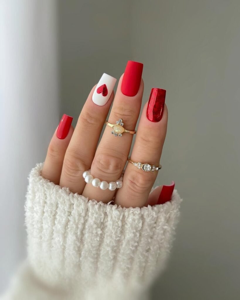 A hand with square-shaped nails featuring red nail polish on most nails and one white nail with a red heart design, showcasing elegant Red Nail Ideas.