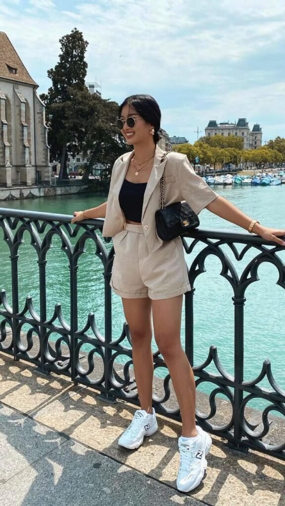  A woman standing on a bridge in Zurich, wearing a beige co-ord short suit with white sneakers and a black crop top — a smart yet relaxed European summer outfit.