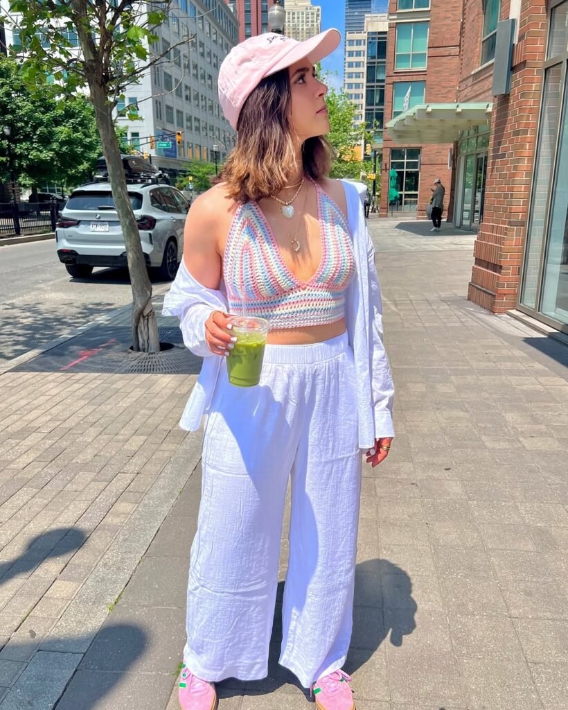  Woman in a pastel rainbow crochet halter top paired with white pants, a white overshirt, pink cap, and sneakers – Crochet Outfits.