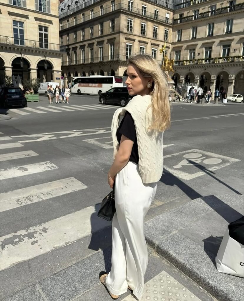  Minimalist stylish work outfit with a black tee and white trousers accessorized with a knit sweater.