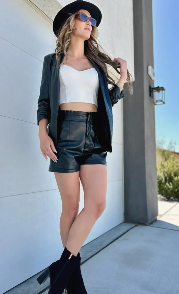 Minimalist Leather Blazer outfit with a structured black blazer, white crop top, black leather shorts, ankle boots, and a fedora hat.