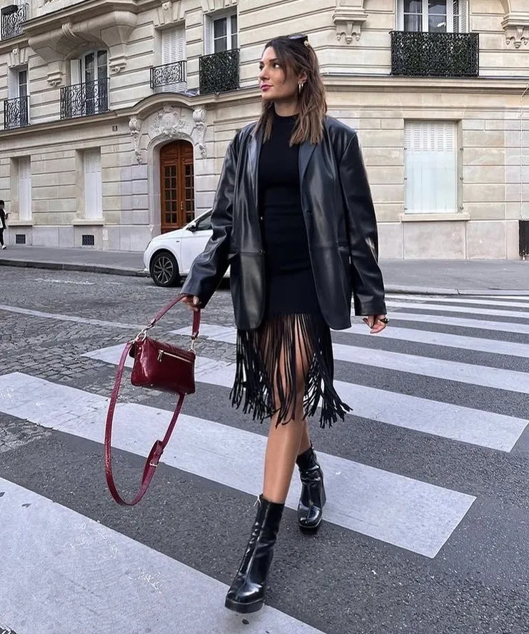 Statement Leather Blazer styled over a black fringe dress, paired with chunky black boots and a burgundy handbag for a bold streetwear edge.