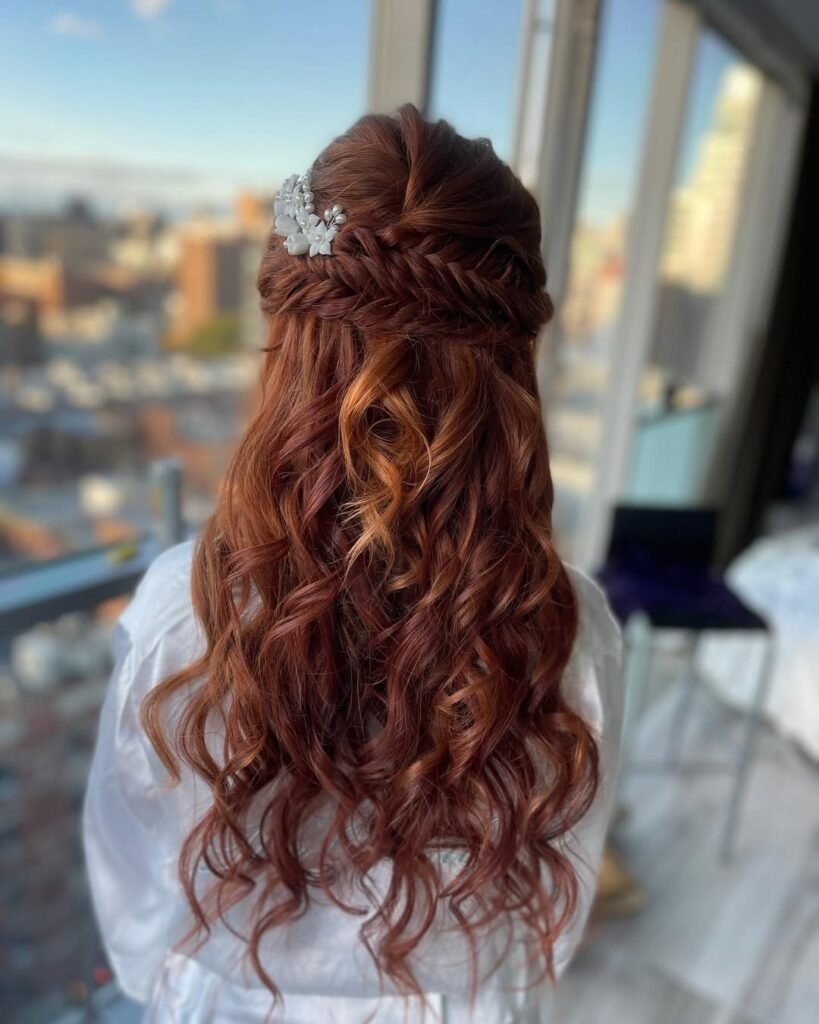 Elegant hairstyle with deep red curls and fishtail braids adorned with floral hair accessories.