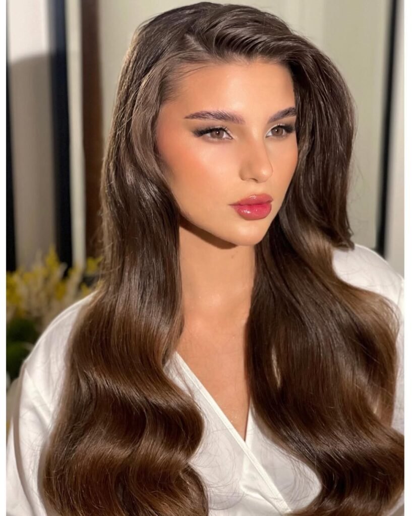 Elegant hairstyle with long, glossy waves and a deep side part for a glamorous look.

