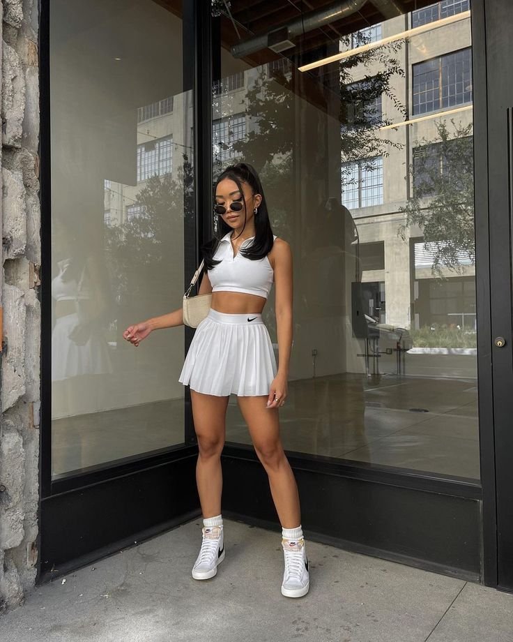Woman wearing a sporty white crop top and white skirt outfit standing outside a building.