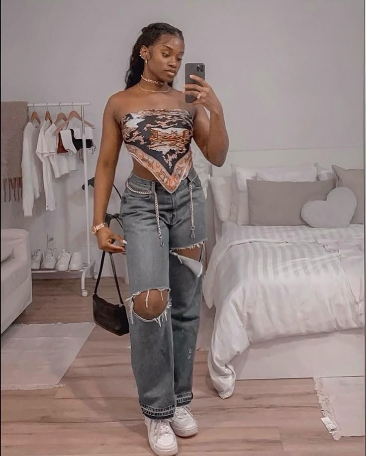 Woman wearing ripped jeans and a printed bandana top posing in a chic bedroom — perfect for casual streetwear vibes. Outfits Casuales.