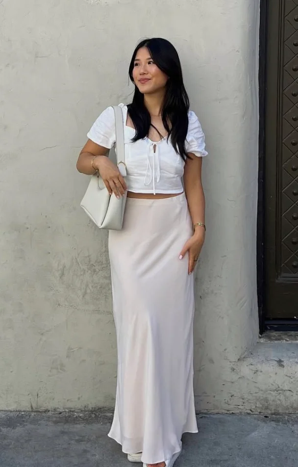 Woman wearing a white crop top paired with a cream slip skirt and white shoulder bag, creating a chic and minimalist look among skirt outfits.
