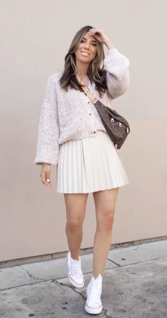 Woman wearing a beige pleated mini skirt paired with a cozy knit sweater and white sneakers, showcasing stylish and comfortable skirt outfits.