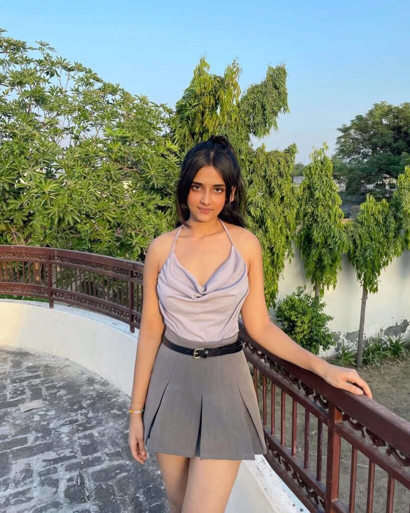 Young woman wearing a pleated gray mini skirt with a stylish sleeveless top, posing outdoors by a railing, showcasing trendy skirt outfits.