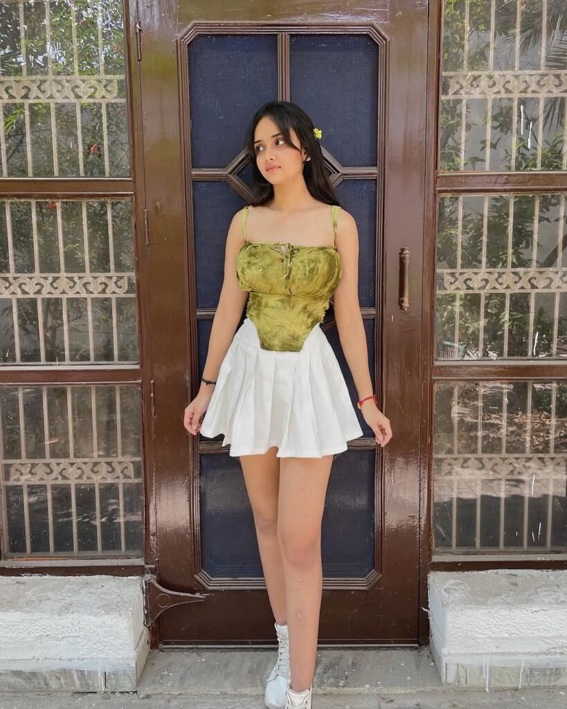 Young woman wearing a white pleated skirt paired with a green velvet corset top and white sneakers, showcasing stylish skirt outfits.