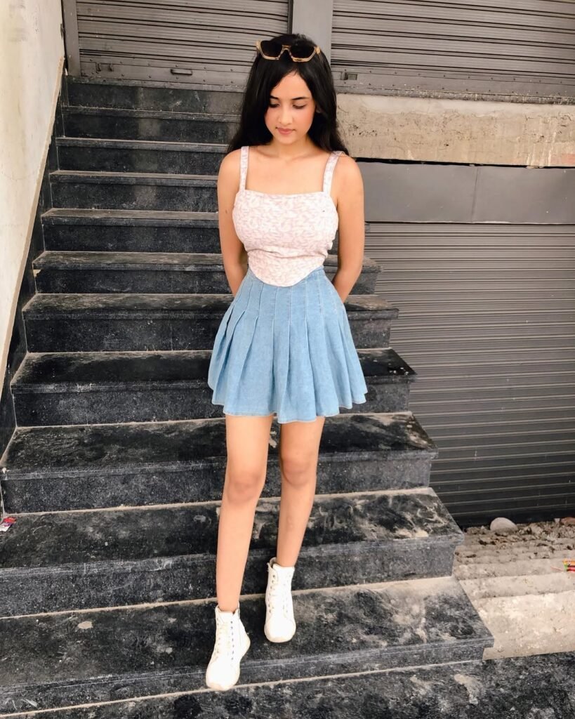 Young woman wearing a blue pleated skirt paired with a sleeveless patterned top and white boots, showcasing trendy skirt outfits.