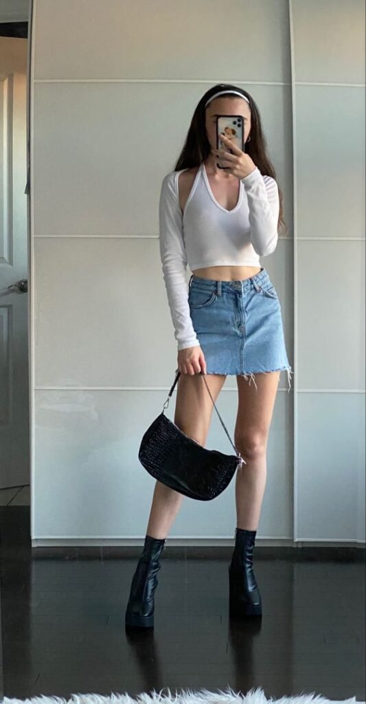 Woman in a white long sleeve crop top paired with a denim skirt outfit posing indoors.