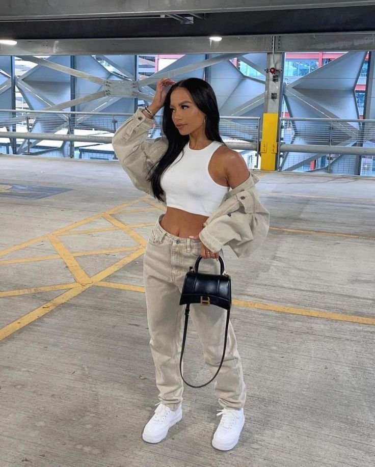 Stylish woman in a white crop top and beige two-piece set with a black handbag in a parking lot. Outfits Casuales.