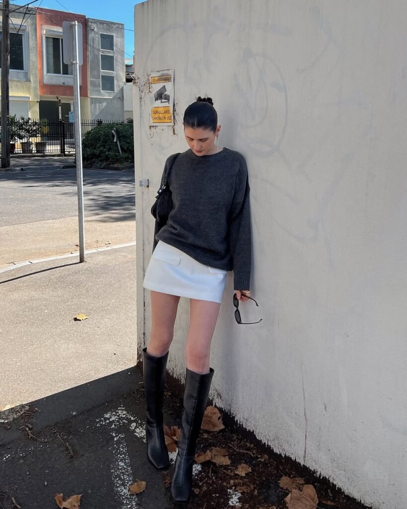 Woman wearing a black sleeveless top and white mini skirt outfit with lace tights outdoors.