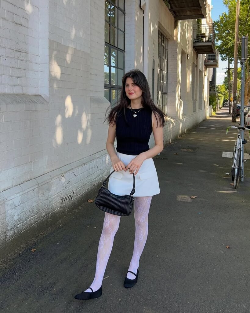 Woman in a chunky white sweater and white skirt outfit standing on brick steps.