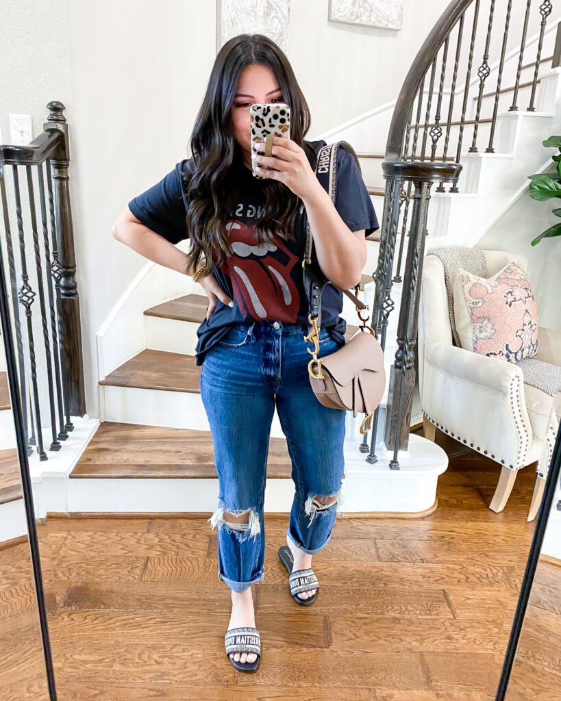 Edgy casual style with a graphic tee and ripped jeans, paired with stylish slides and a beige shoulder bag. Outfits Casuales.