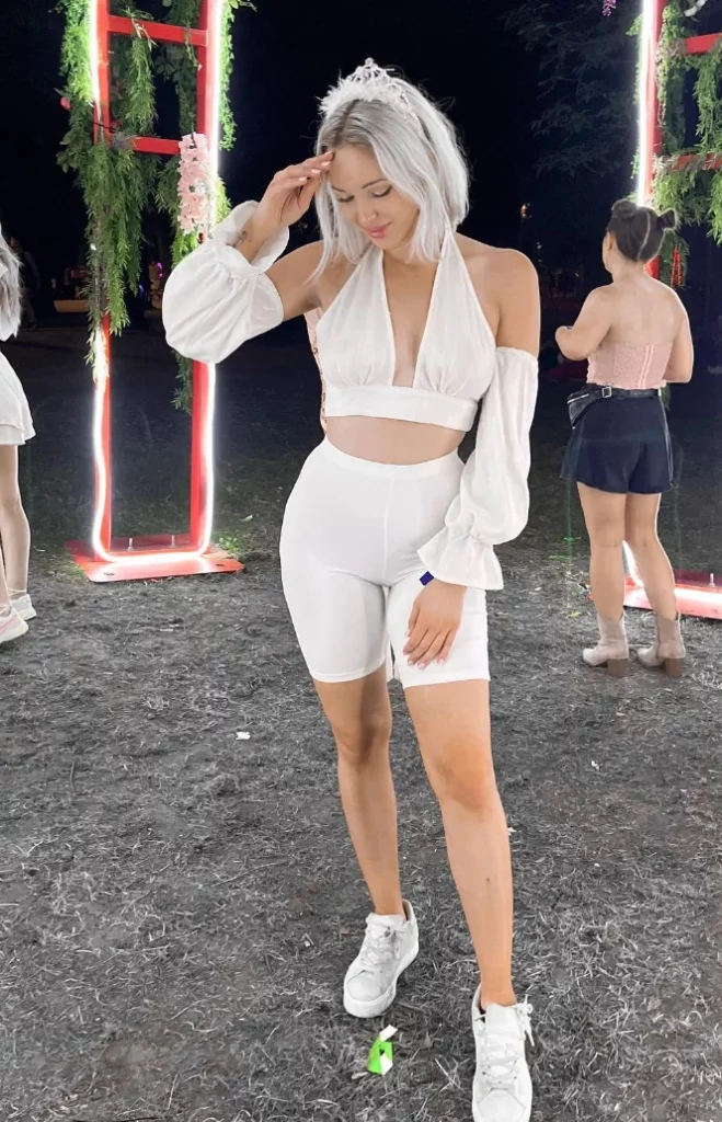 All-white festival-ready biker shorts outfit with a halter crop top and long sleeves, styled with white sneakers and a tiara.