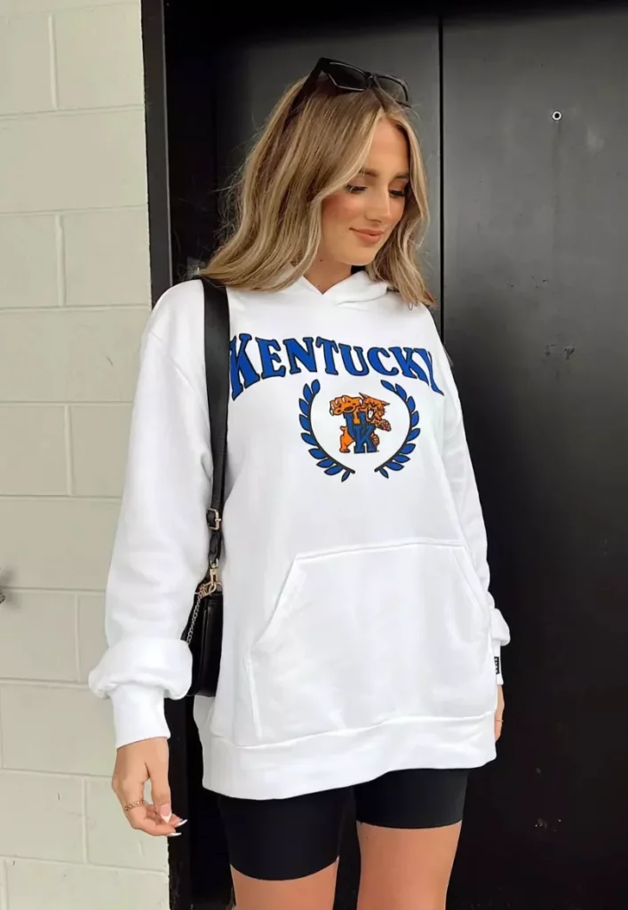 Laid-back look with an oversized white “Kentucky” hoodie and classic black biker shorts outfit, accessorized with a black shoulder bag.