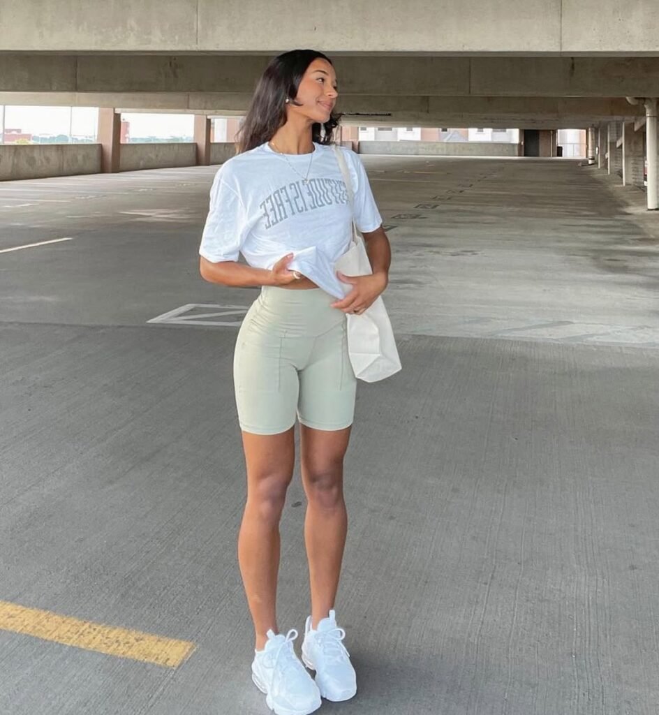 Woman wearing light green biker shorts with white t-shirt and white sneakers standing in an open parking garage, Biker Shorts outfits.