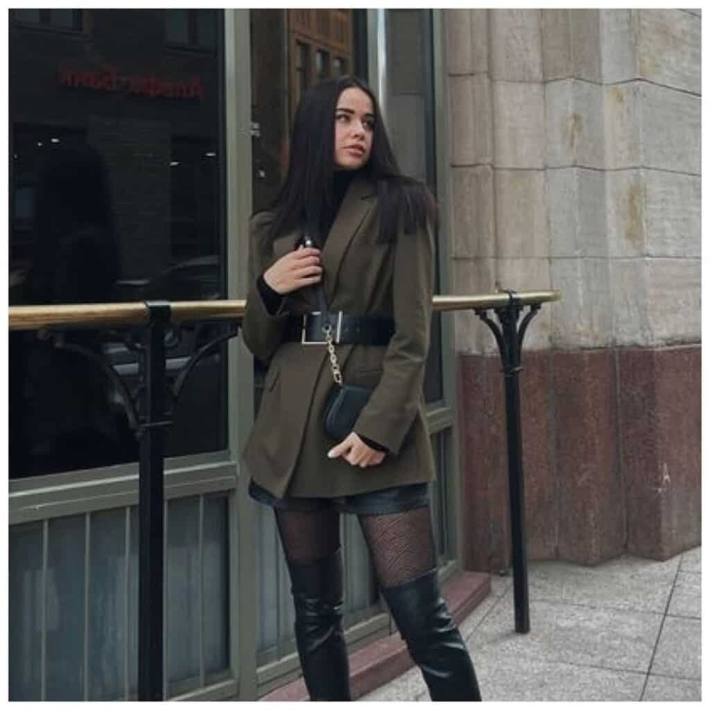 Stylish blazer outfit with a woman in a dark brown oversized blazer paired with black knee-high boots, sitting indoors in a modern restaurant.