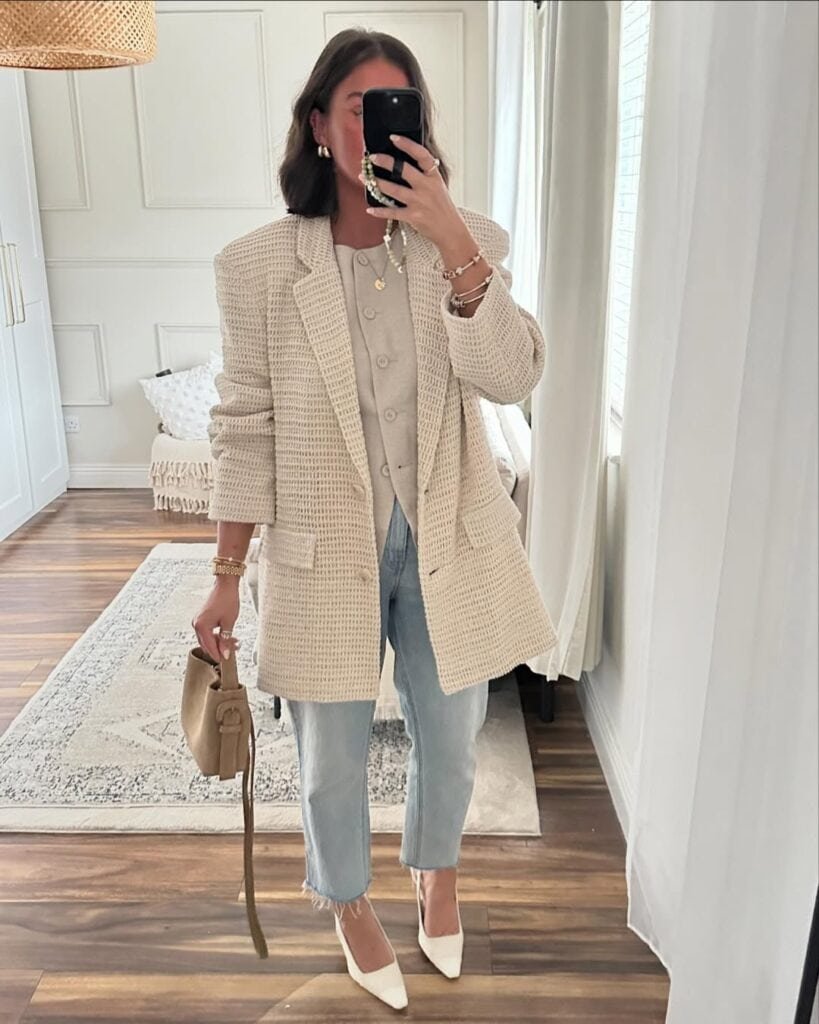 Woman wearing a chic beige blazer outfit paired with light blue jeans and white heels, showcasing a trendy blazer outfit look.