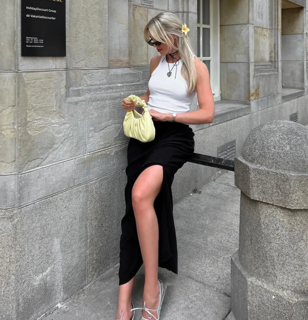 Chic Casual Summer Outfits featuring a white sleeveless top paired with a black high-slit skirt, accessorized with strappy heels and a pastel handbag.