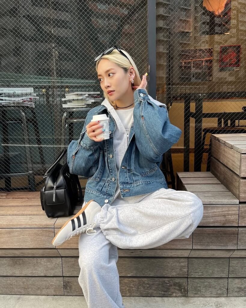 Adidas Samba Outfits featuring a denim jacket layered over a white sweatshirt with light grey joggers, accessorized with a black leather backpack and classic Adidas Samba sneakers.