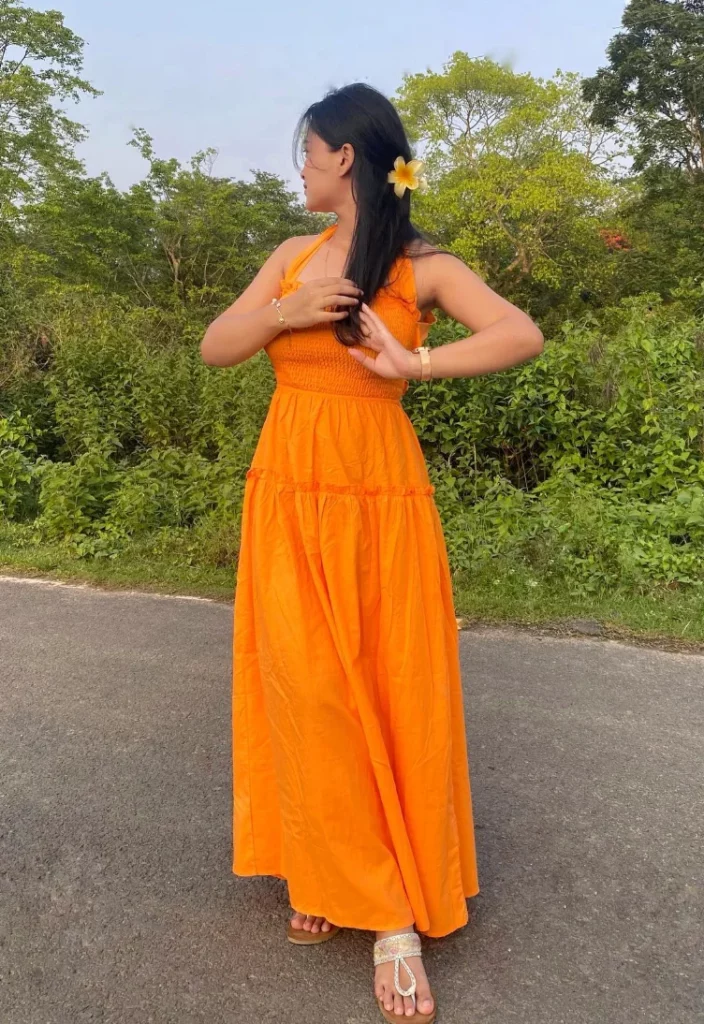 Woman wearing an orange halter maxi dress and barefoot sandals with a flower in her hair, showcasing a breezy and colorful modest summer outfit.
