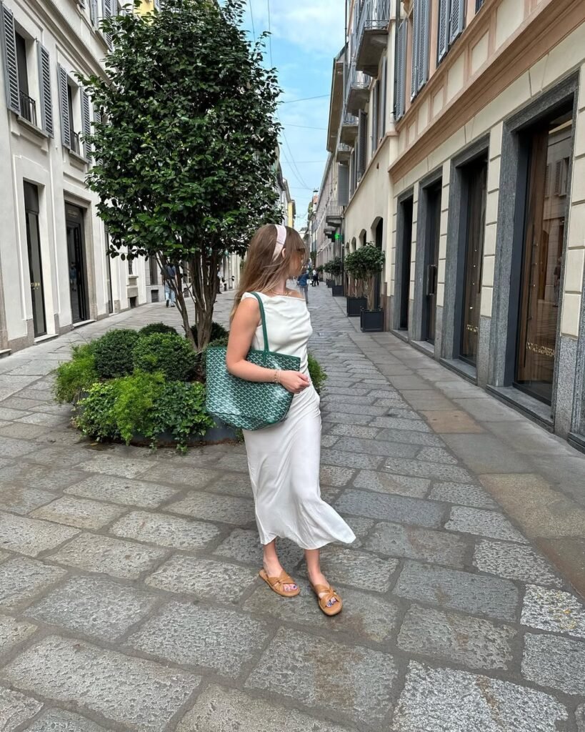 Sleek and refined Summer Outfits with a satin white dress, flat sandals, and a pastel pink headband, captured on a European-style street.