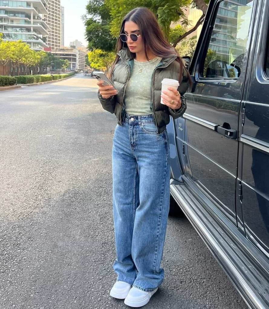 Relaxed wide leg pants outfit with mid-wash denim jeans, a cropped padded jacket, and white sneakers for a casual city stroll.