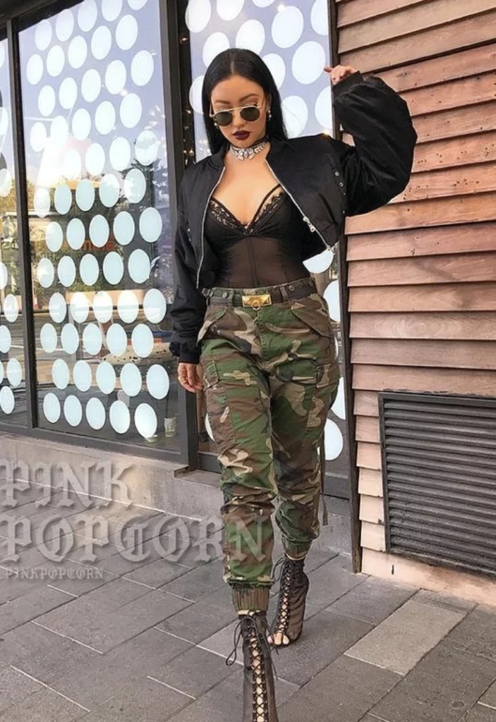 Camouflage Pants Outfit featuring a black lace bodysuit, cropped bomber jacket, and lace-up heels, styled with edgy accessories and sunglasses.