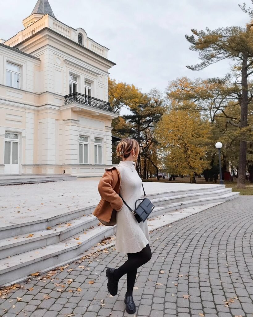 Autumn-inspired coffee date outfit with a beige sweater dress, brown coat, black boots, and a crossbody bag.