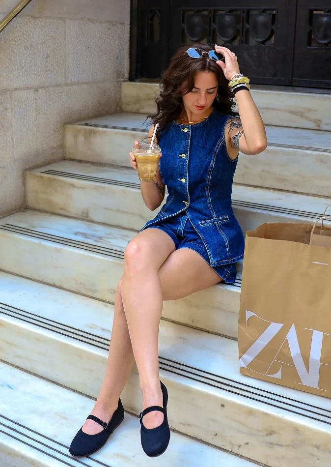 Woman sitting on stairs in a sleeveless denim romper—this outfit is more casual than modest but styled for a breezy summer day.