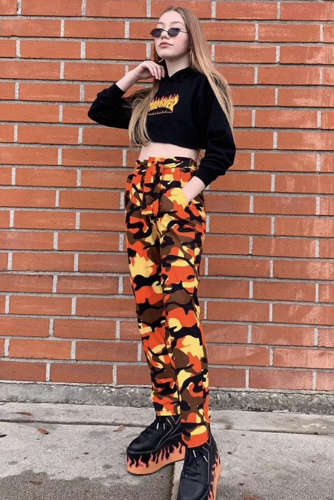 Camouflage Pants Outfit in bold orange and yellow tones, paired with a cropped graphic hoodie and flame-patterned platform shoes for a vibrant street style look.