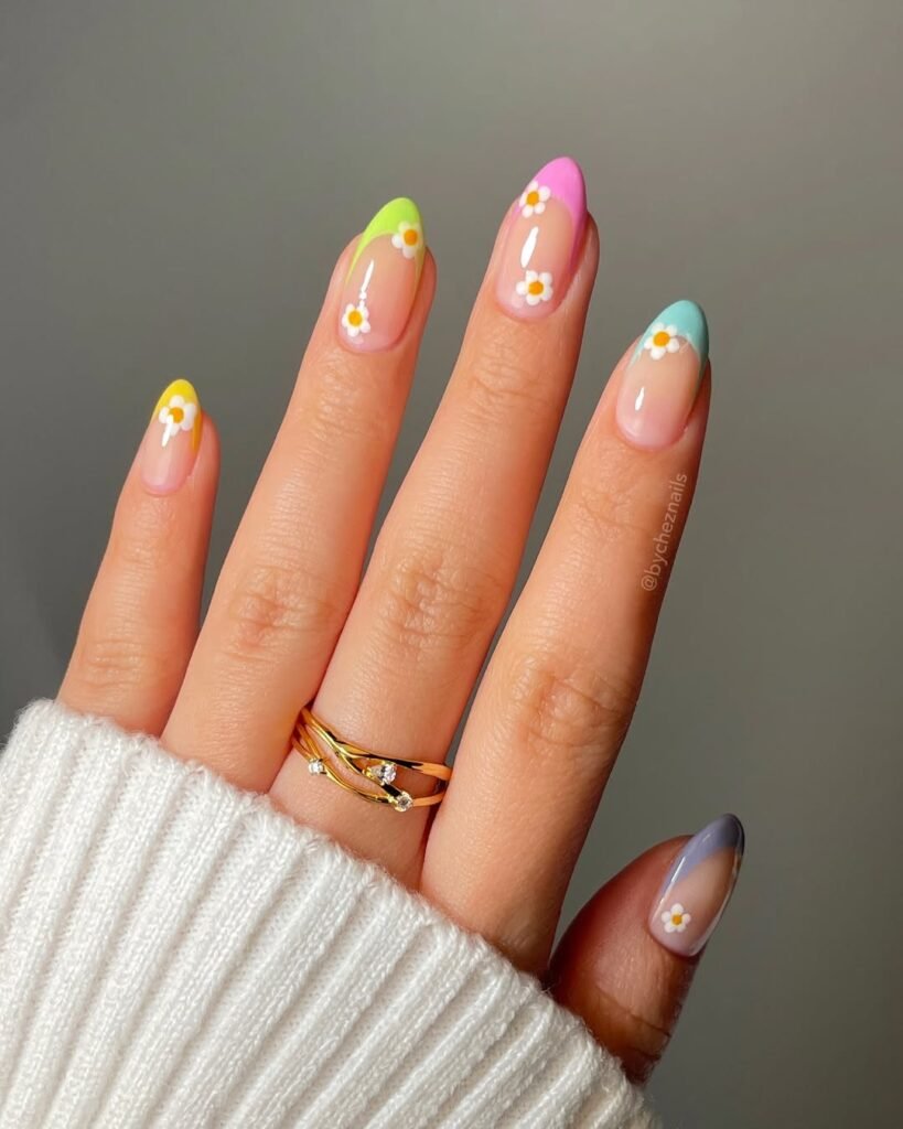 Spring Nail Ideas in vibrant French tips with rainbow pastel colors and cute white daisy accents over a nude base.