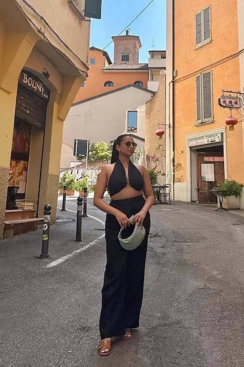 Bold Summer Vacation Outfit with an all-black halter top and wide-leg pants, accessorized with sunglasses and a round woven bag.